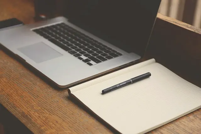 photo représentant, un ordinateur, un stylo, et un carnet ouvert sur un bureau
